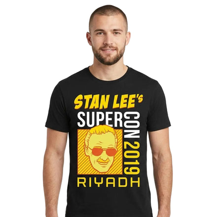 A man wearing a black t-shirt with a yellow and white graphic print that reads 'STAN LEE'S SUPERCON 2019 RIYADH' alongside a stylized illustration of Stan Lee wearing sunglasses.