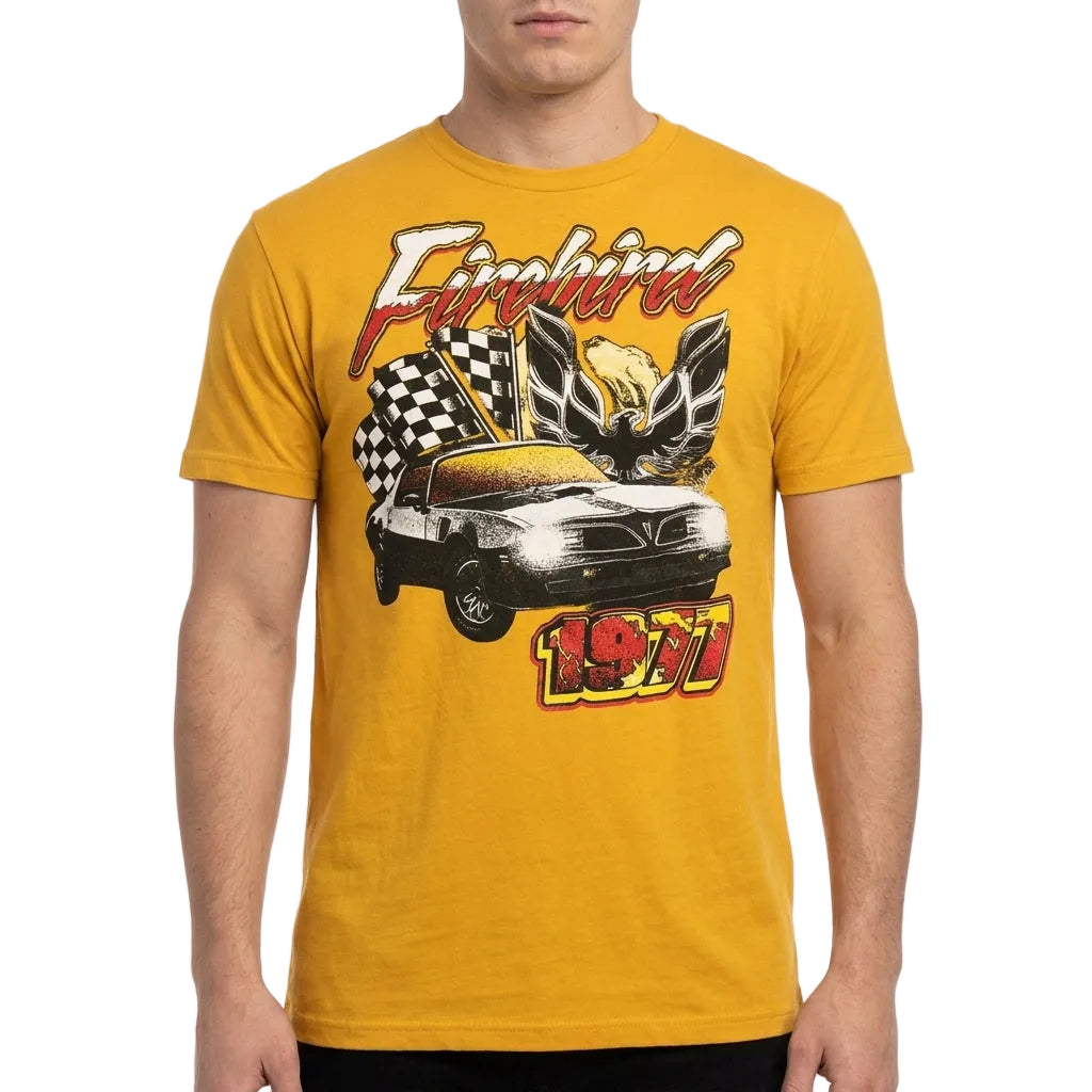 A man wearing a golden yellow t-shirt with a vintage-style graphic of a 1971 Firebird car, checkered flags, and a winged emblem on the front.