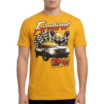 A man wearing a golden yellow t-shirt with a vintage-style graphic of a 1971 Firebird car, checkered flags, and a winged emblem on the front.