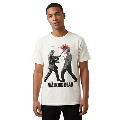 A man wearing a white graphic t-shirt featuring a black and red print from 'The Walking Dead' on a light gray studio background.