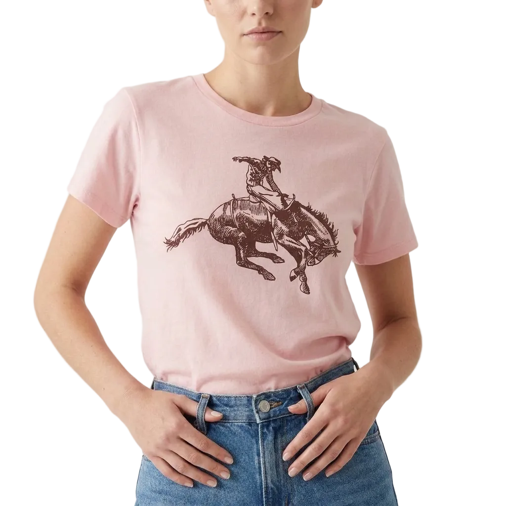 A model wearing a light pink crewneck t-shirt with a dark brown graphic of a cowboy riding a bucking horse, paired with blue jeans against a plain light background.