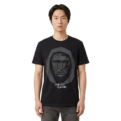 A man wearing a black short-sleeve t-shirt with a gray low-poly face graphic and the text 'SQUID GAME' printed on the front, paired with gray jeans, against a light gray studio background. 