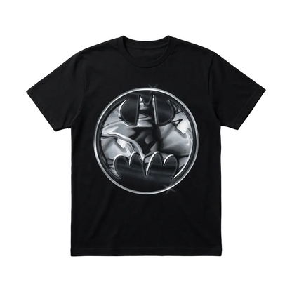 A black short-sleeve crewneck t-shirt featuring a circular metallic silver and black Batman graphic printed on the chest, displayed flat against a textured gray background.