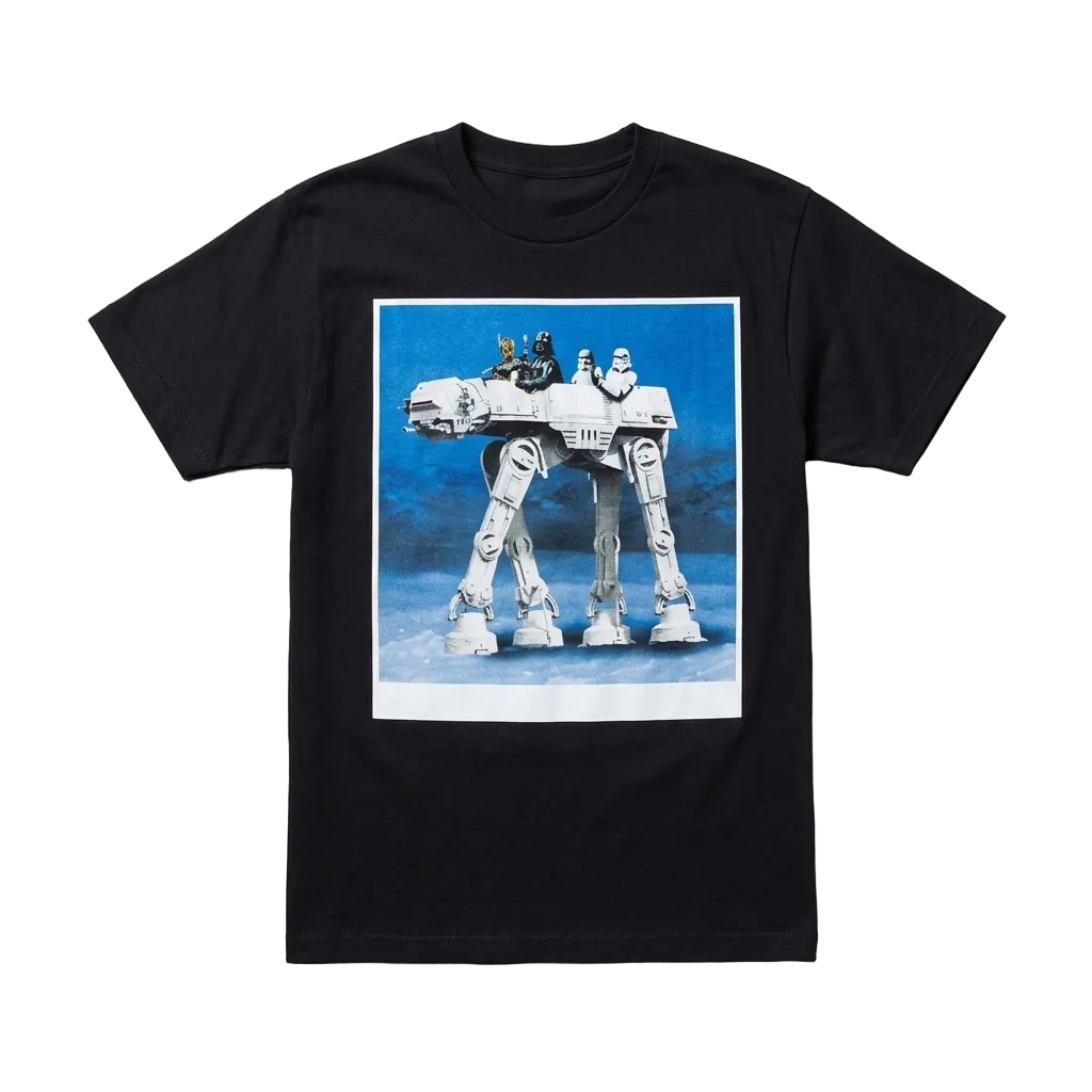 A black short-sleeve crewneck t-shirt featuring a large graphic print of an AT-AT walker on a blue background, laid flat on a textured gray surface. 