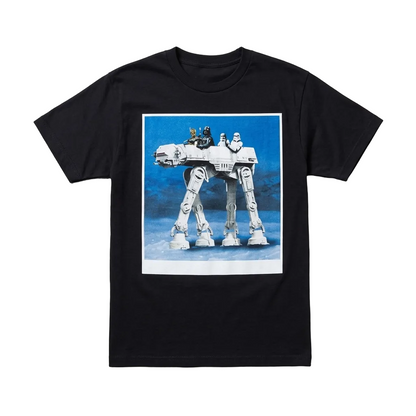 A black short-sleeve crewneck t-shirt featuring a large graphic print of an AT-AT walker on a blue background, laid flat on a textured gray surface. 
