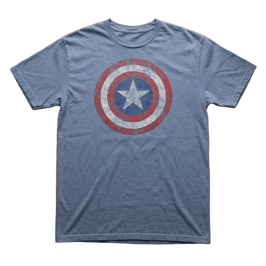 A heather blue crewneck t-shirt featuring a distressed Captain America shield graphic on the chest, laid flat on a light wood desk surrounded by comic book frames and Funko Pop figures.