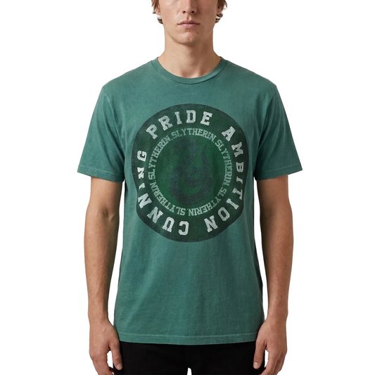 A man wearing a green crewneck t-shirt with a circular Slytherin-themed graphic on the front, featuring the words 'Pride', 'Ambition', and 'Cunning' in white around a dark green crest.