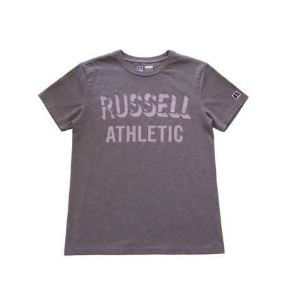 Gray t-shirt with 'Russell Athletic' text on a light gray surface with flowers and a mug. 