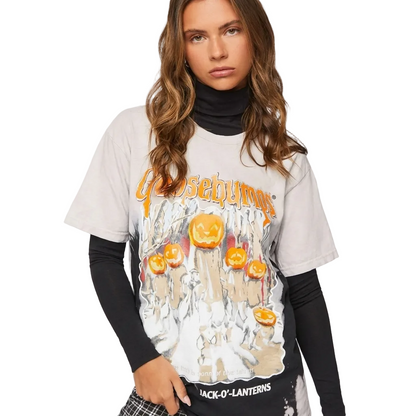 A woman wearing a Goosebone Halloween graphic t-shirt over a black turtleneck and black long-sleeve undershirt, posed against a solid off-white background.