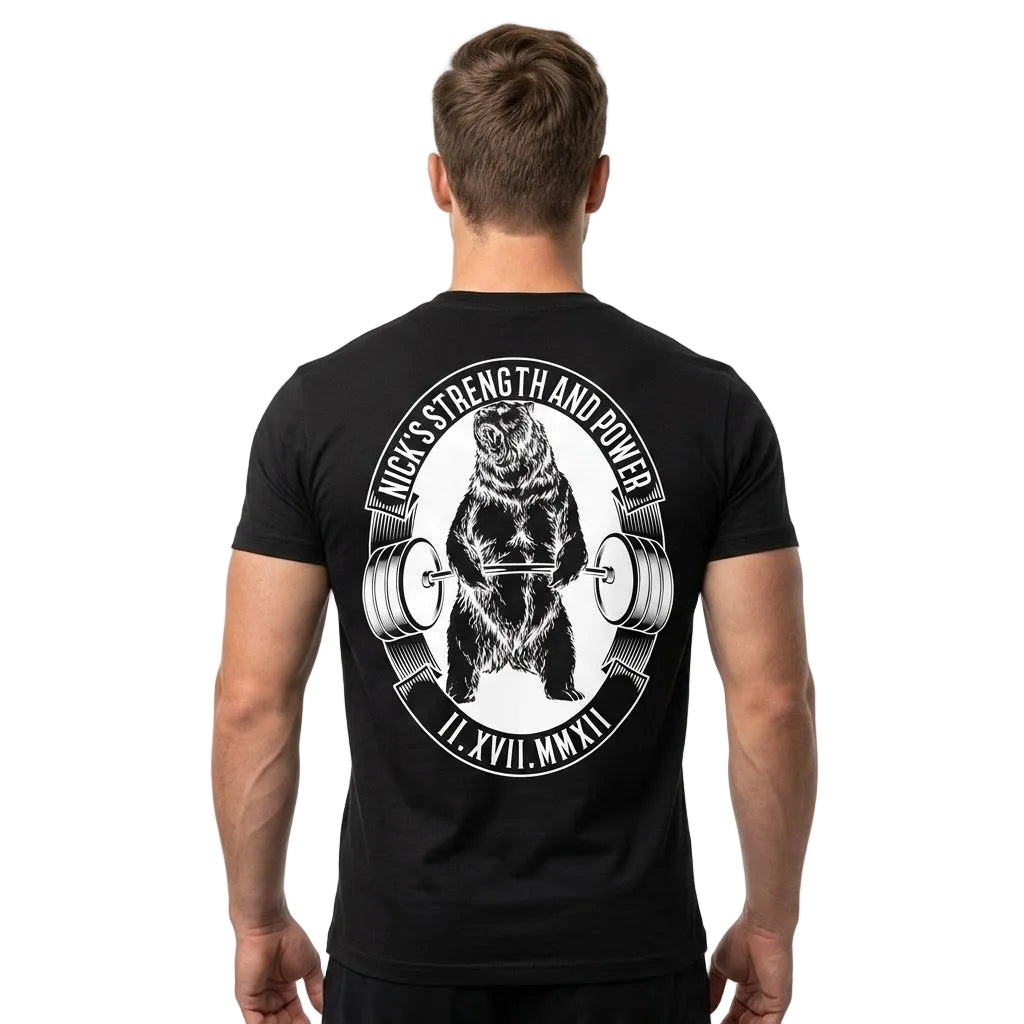 A man viewed from behind wearing a black t-shirt with a large white graphic print of a bear lifting a barbell on the back. The text reads 'WECK YOUR STRENGTH AND POWER' and 'IL.